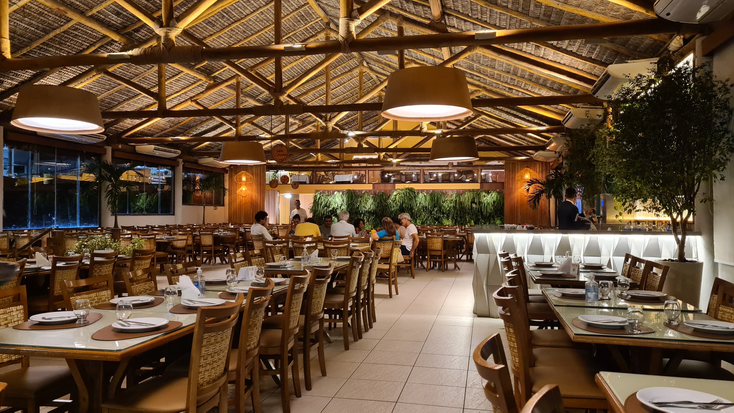 Interior of Cabana do Sol restaurant in São Luís at night, wooden beams and thatched roof, diners at tables