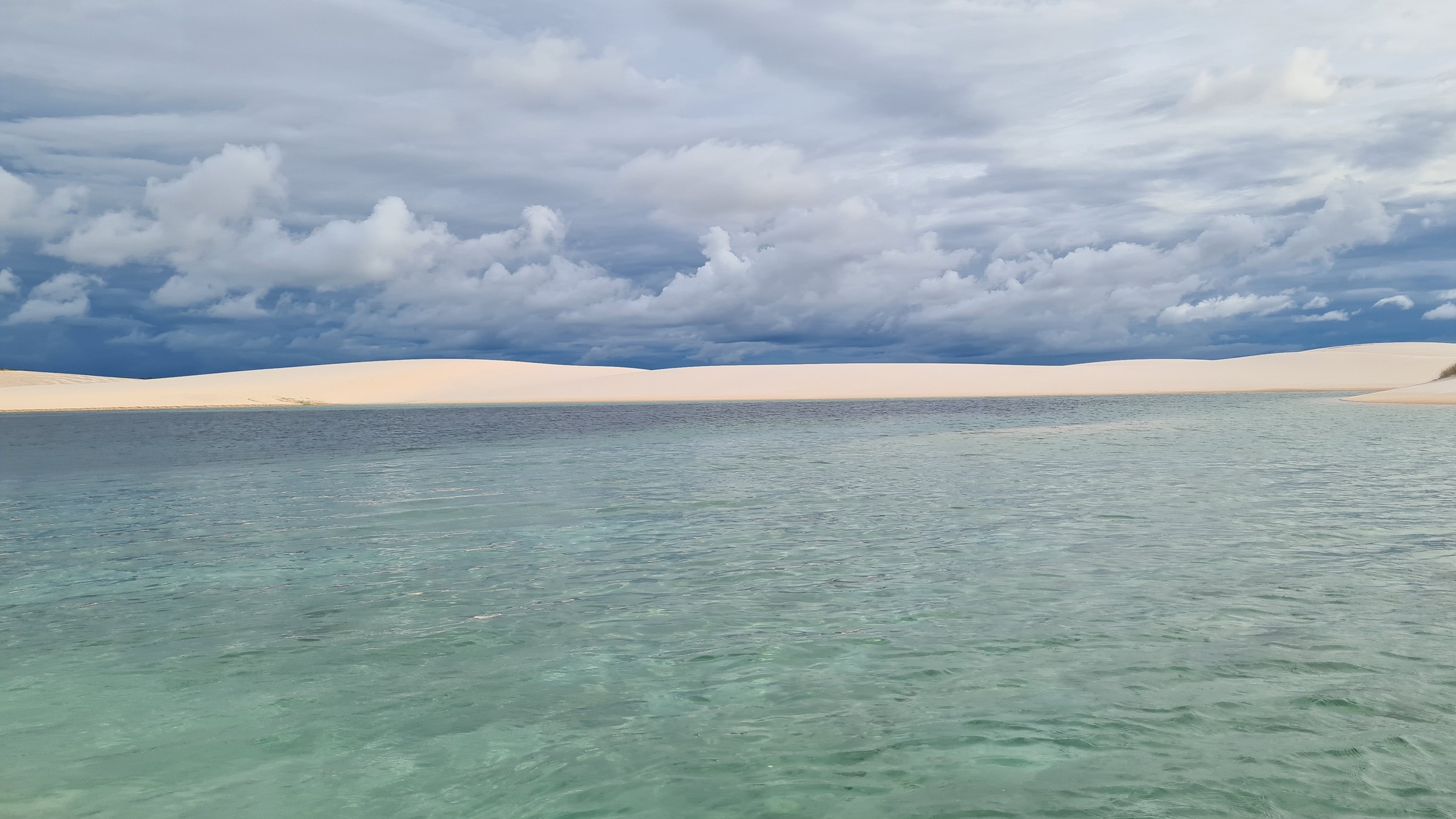 Turquoise lagoon among white sand dunes near Povoado Massangano under a dramatic dark storm sky