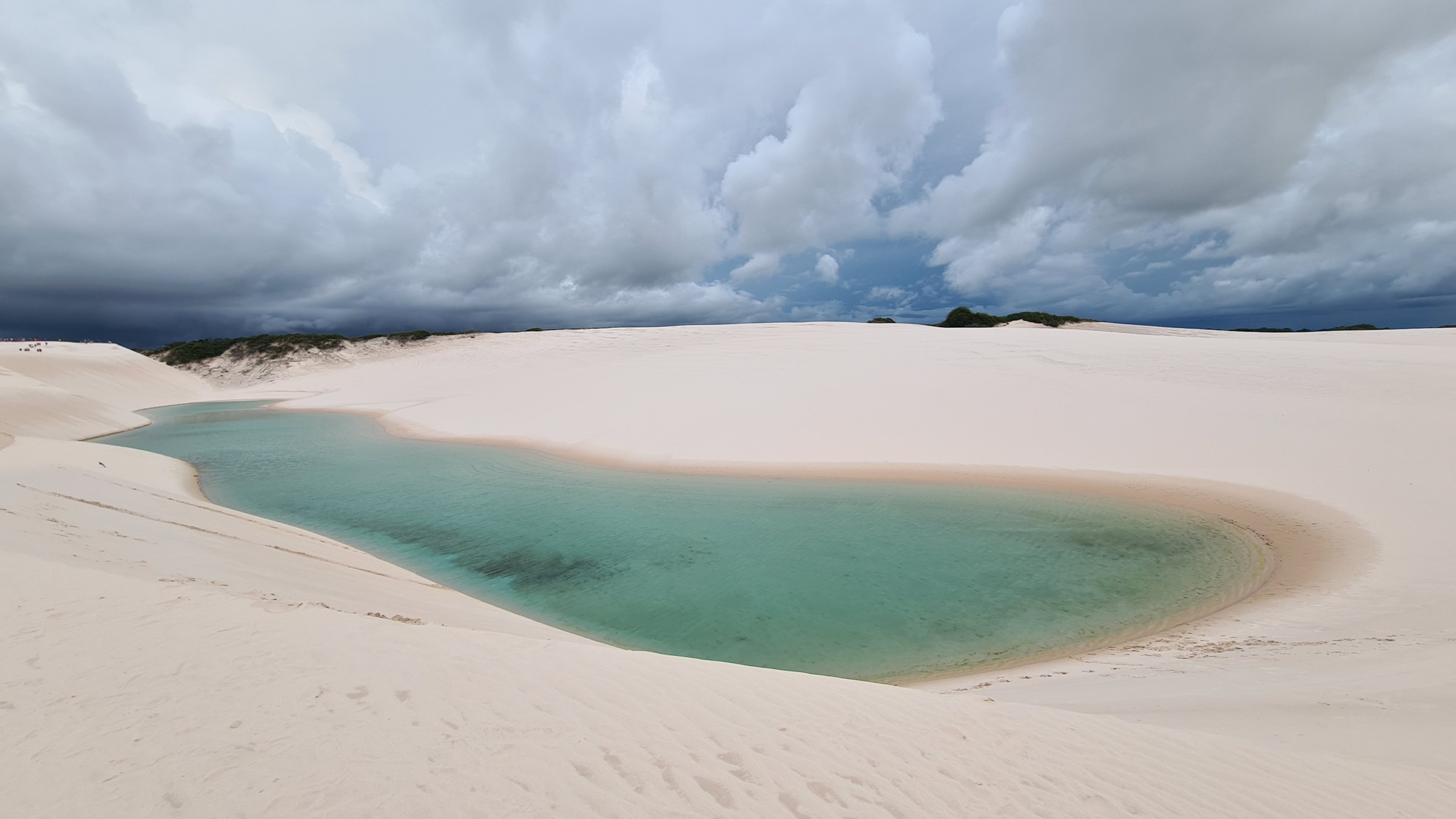 Wide sweep of a teal-colored lagoon curving between white dunes under a stormy sky