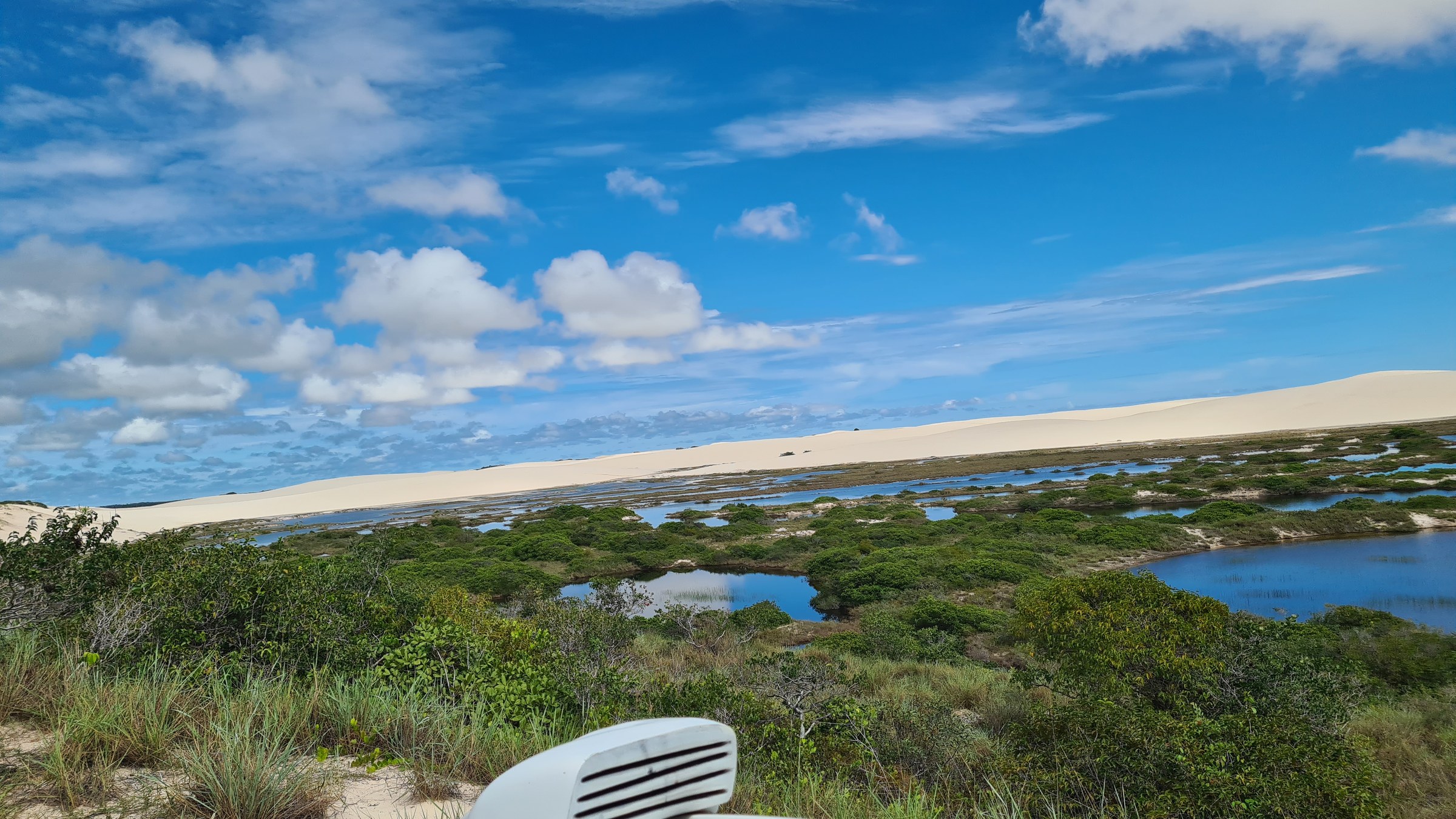 Panoramic view over a marshy dune wetland dotted with small pools and green scrub, near Ponta do Mangue